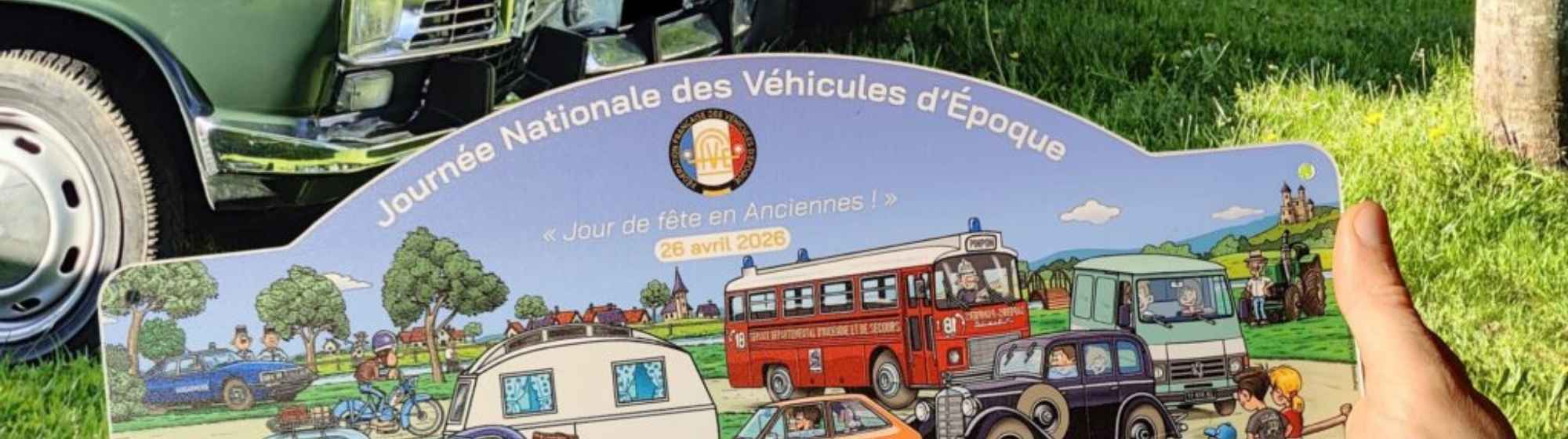 Line of vintage cars on grass with an illustrated poster of the National Vintage Vehicles Day