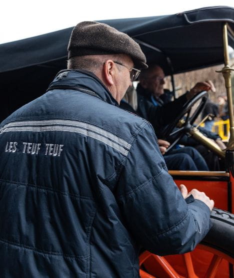 back of a man wearing a blue jacket and in front of a vintage red and black car