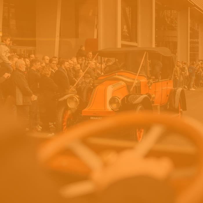 close-up of a steering wheel in front of a vintage car with a crowd