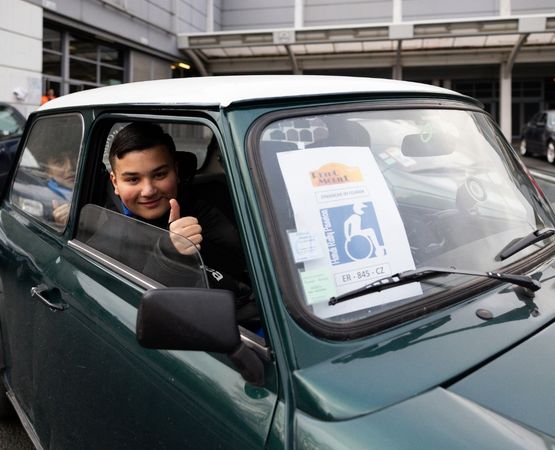 Jeune homme souriant assis dans une voiture ancienne avec un badge PMR à l'avant.