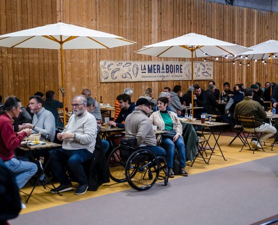 Salle de restauration avec des visiteurs assis à des tables sous des parasols, prenant une pause lors d'un salon.
